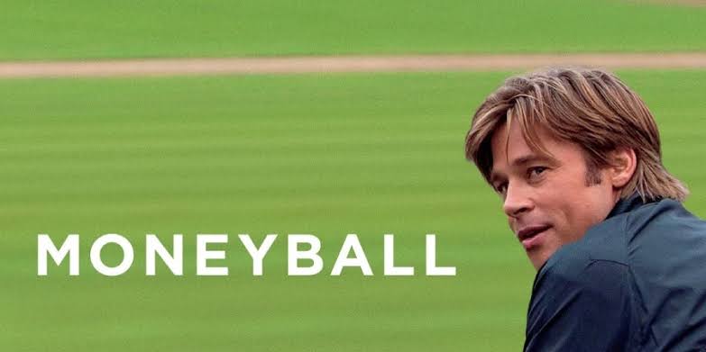 Brad Pitt como Billy Beane em campo de beisebol verde, olhando por cima do ombro. Título "MONEYBALL" em branco.
