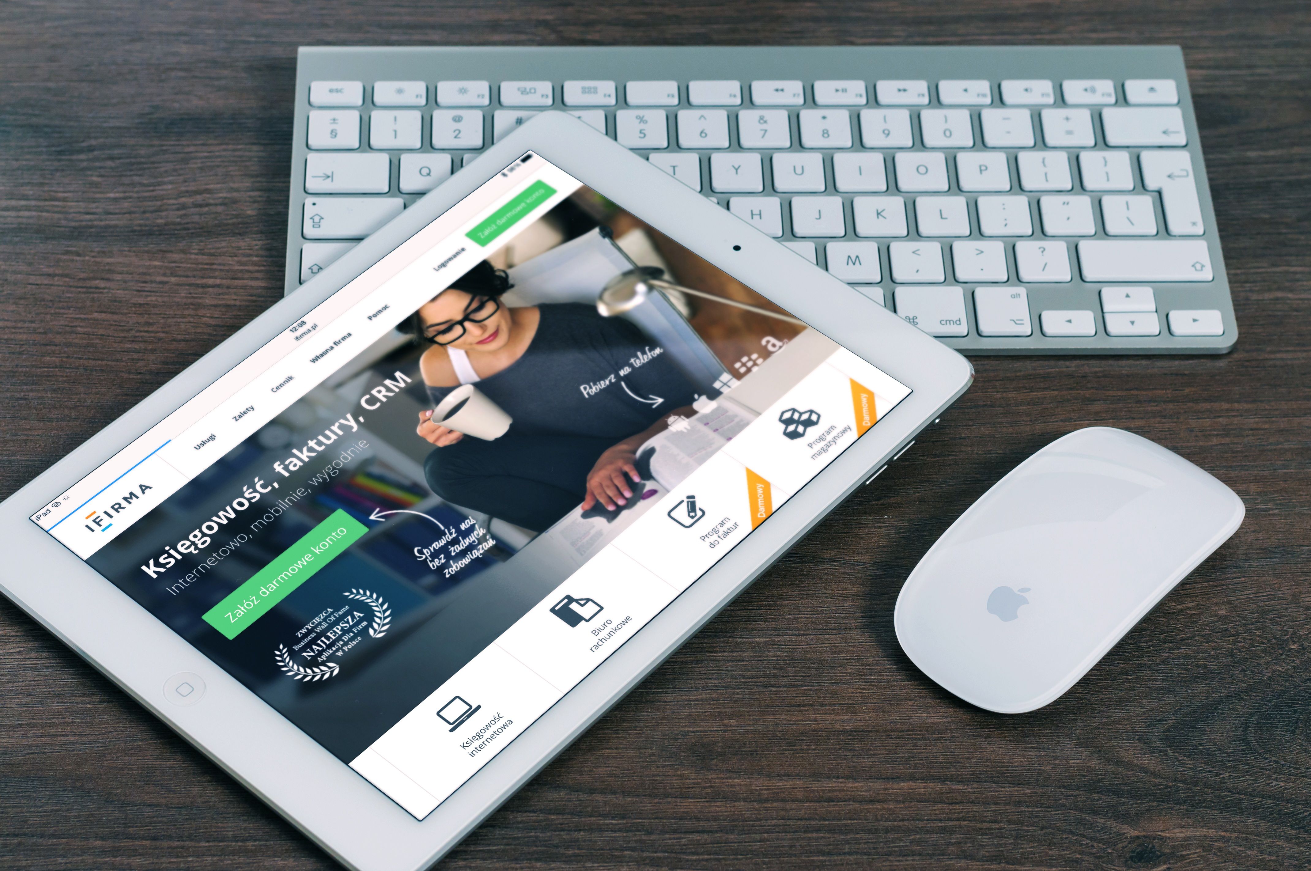 Tablet branco com site de contabilidade polonês, teclado e mouse brancos em mesa de madeira escura.